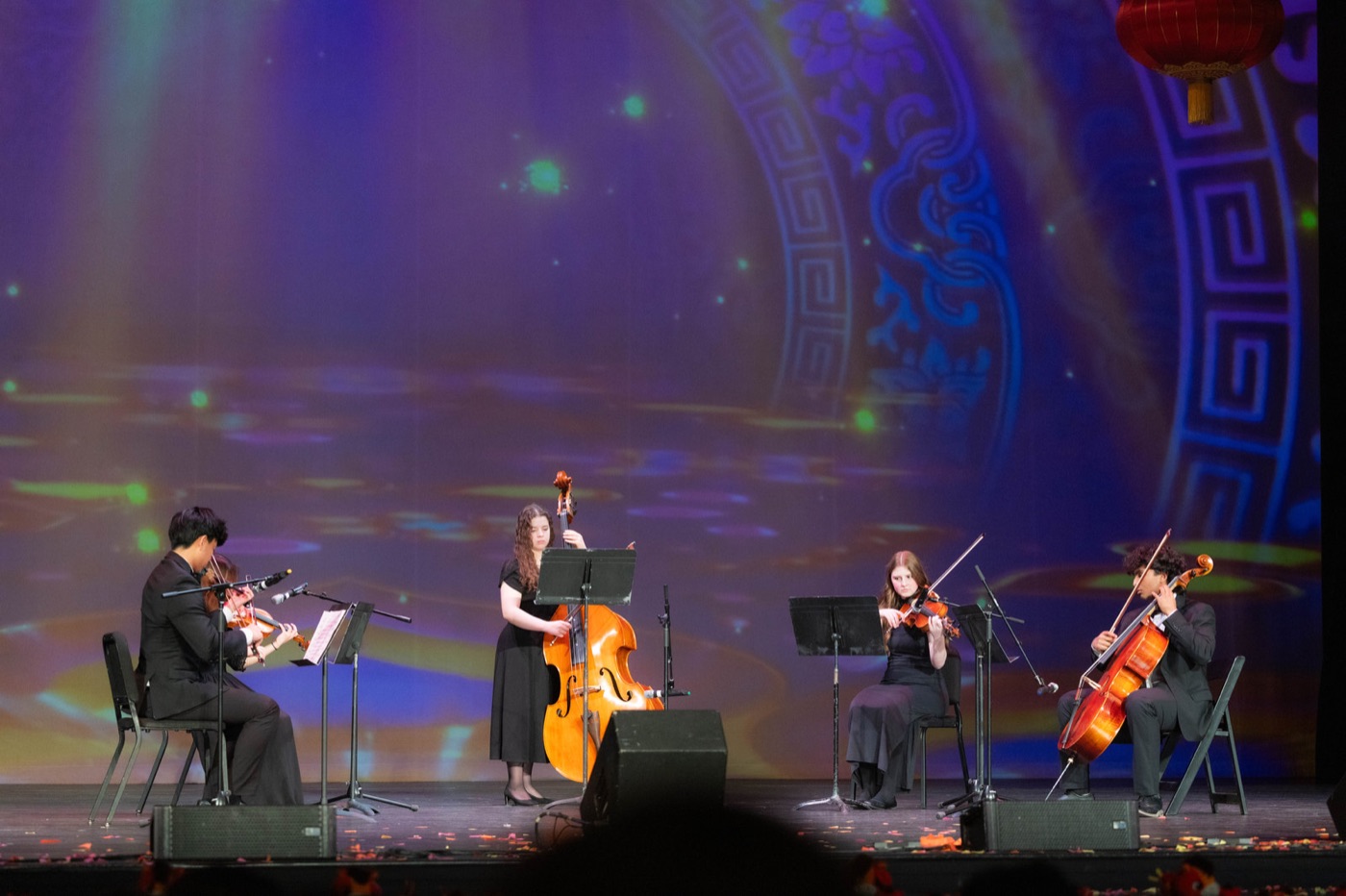 Piano and string musicians perform beneath blue stage lights