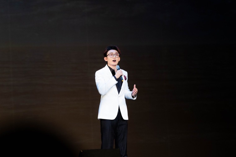 A vocalist in a white jacket performs under stage lights