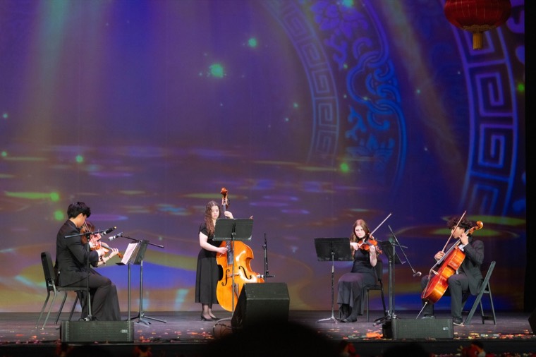 Piano and string musicians perform beneath blue stage lights